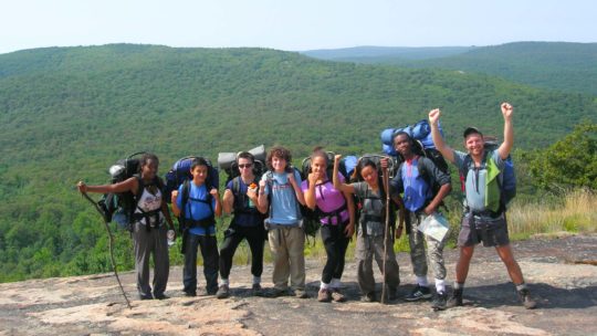 Campers on a camping trip taking a group photo with their backpacks on